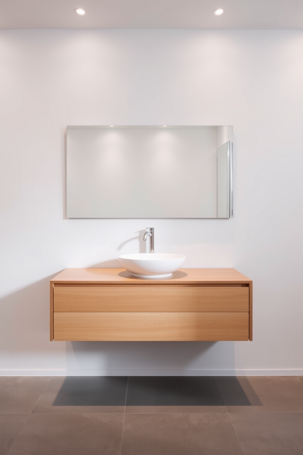 A sleek floating vanity is mounted against a clean white wall, showcasing a minimalist design with a natural wood finish. Above the vanity, a large frameless mirror reflects the soft ambient lighting from recessed fixtures, enhancing the modern aesthetic. The floor features large format gray tiles that complement the vanity while providing a contemporary touch. A stylish vessel sink sits atop the vanity, accompanied by a brushed nickel faucet, adding a touch of elegance to the overall design.