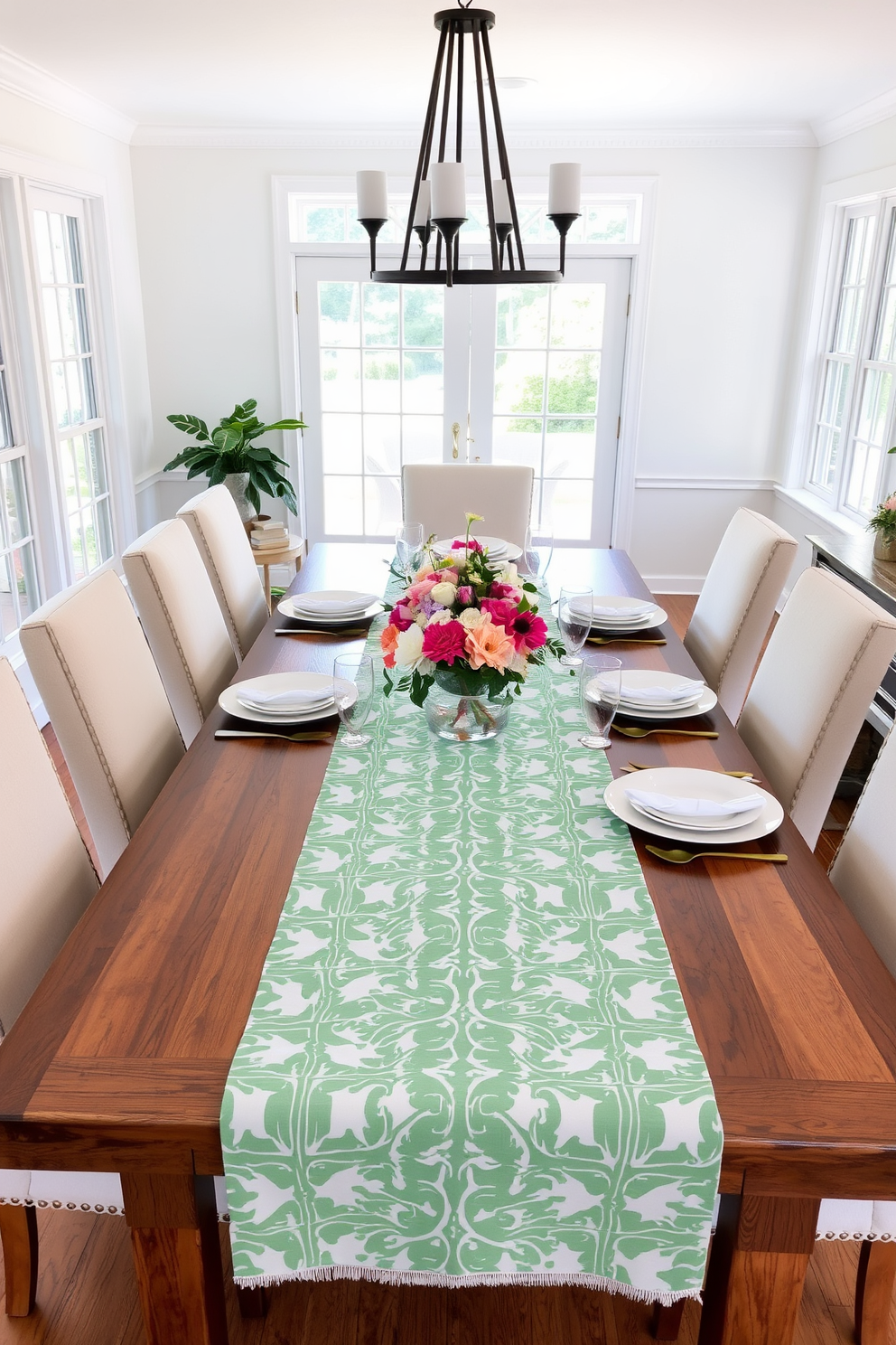 A bright and airy dining room features a large wooden table set for a summer gathering. The table is adorned with a bold patterned table runner that adds a vibrant touch to the white tableware and fresh floral centerpiece. Surrounding the table are comfortable upholstered chairs in a soft pastel hue. Large windows allow natural light to flood the space, enhancing the cheerful atmosphere of the summer decor.