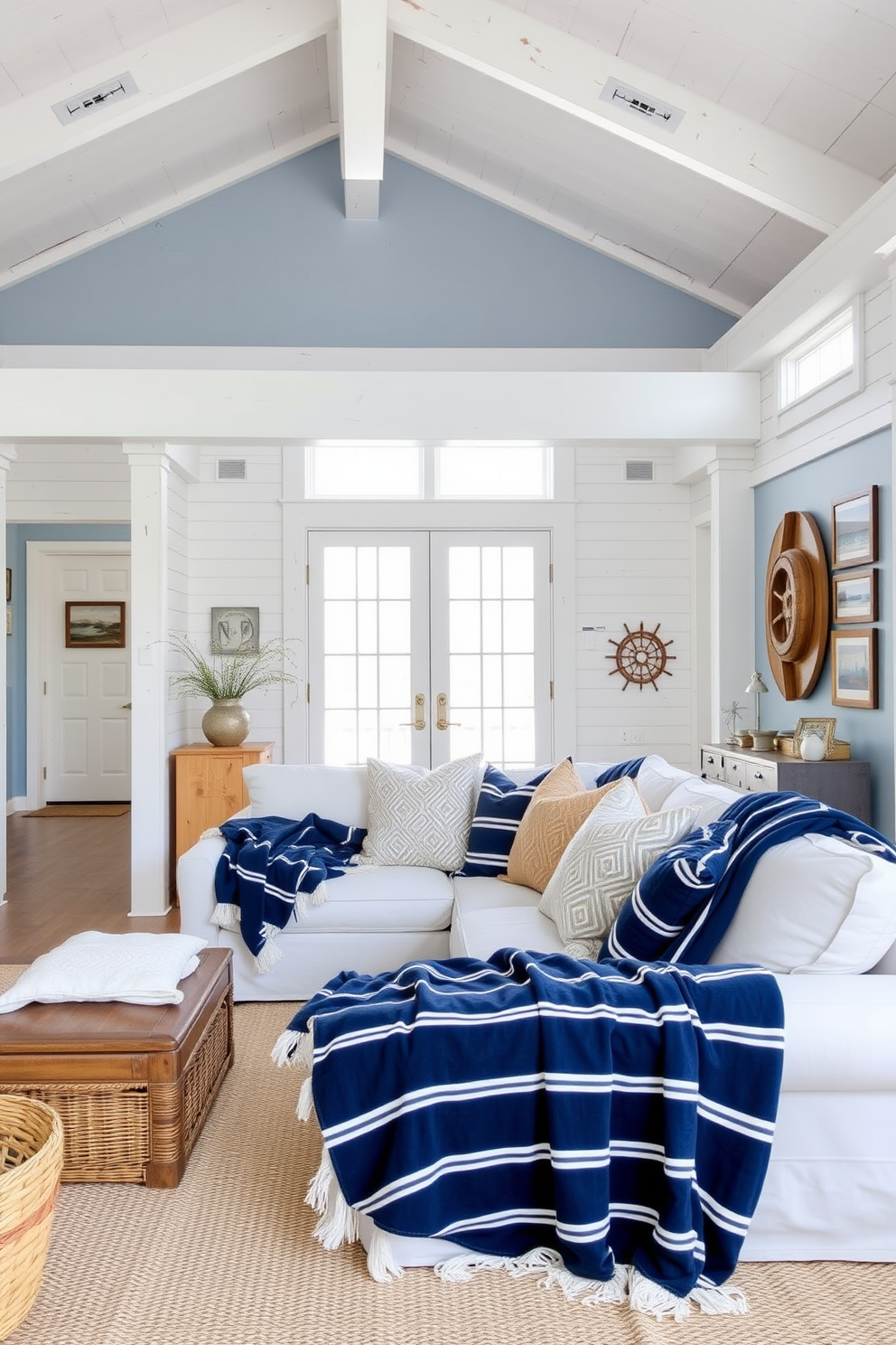 A bright and airy summer loft with a coastal theme. The open space features whitewashed wood beams and large windows that let in natural light, while the walls are adorned with soft blue accents. A comfortable sectional sofa is draped with navy and white striped throw blankets, complemented by an assortment of textured pillows in sandy tones. Nautical decor elements such as a ship wheel and framed ocean prints add charm and character to the space.