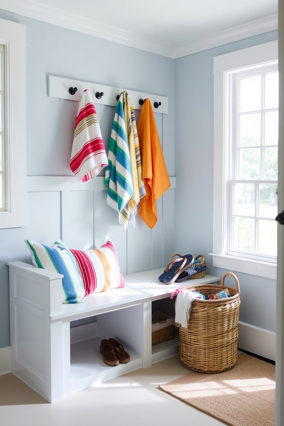 A bright and airy summer mudroom features a spacious bench with built-in storage underneath for beach towels. The walls are painted in a soft coastal blue, and large windows allow natural light to flood the space, creating a welcoming atmosphere. Colorful beach towels hang neatly on hooks, ready for quick drying after a day at the beach. A woven basket filled with flip-flops sits beside the entrance, adding a touch of casual charm to the decor.