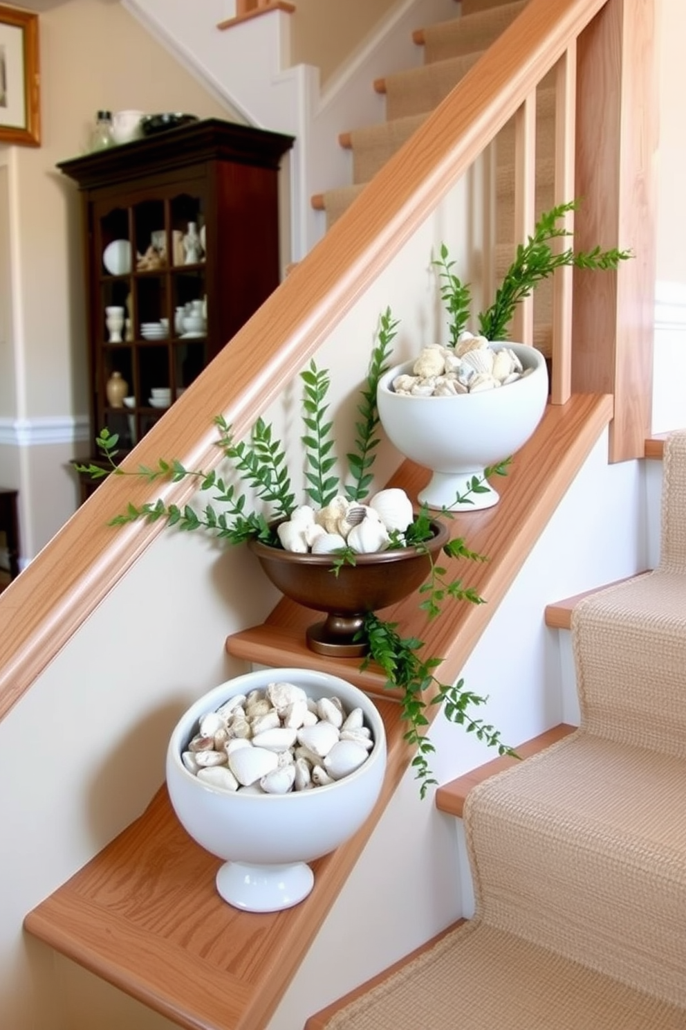 A stylish staircase adorned with decorative bowls filled with various seashells creates a coastal vibe. The bowls are strategically placed along the staircase railing, adding a touch of summer charm to the space. The staircase itself features a light wood finish with a subtle runner that complements the seashell decor. Fresh greenery is interspersed with the bowls to enhance the summer aesthetic and bring a breath of fresh air indoors.